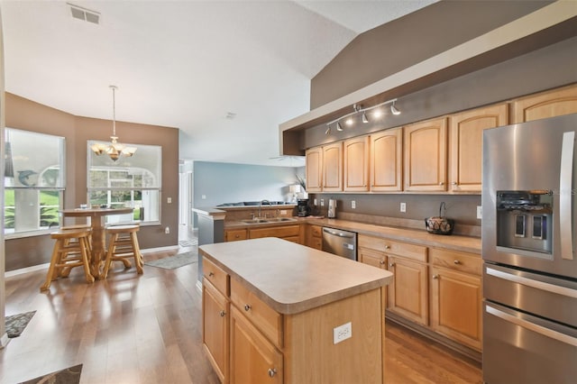 kitchen featuring hanging light fixtures, light wood-type flooring, appliances with stainless steel finishes, kitchen peninsula, and a kitchen island