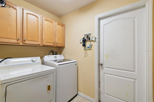 laundry room featuring light tile patterned floors, a textured ceiling, cabinets, and washing machine and clothes dryer