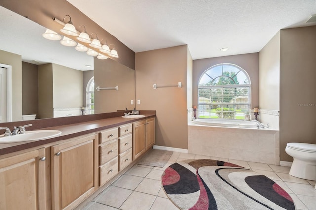 bathroom featuring tiled bath, vanity, toilet, tile patterned floors, and a textured ceiling