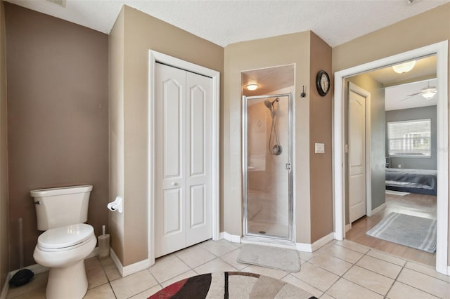 bathroom with ceiling fan, tile patterned flooring, a textured ceiling, toilet, and walk in shower