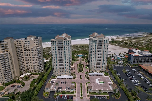 aerial view at dusk featuring a water view and a view of the beach