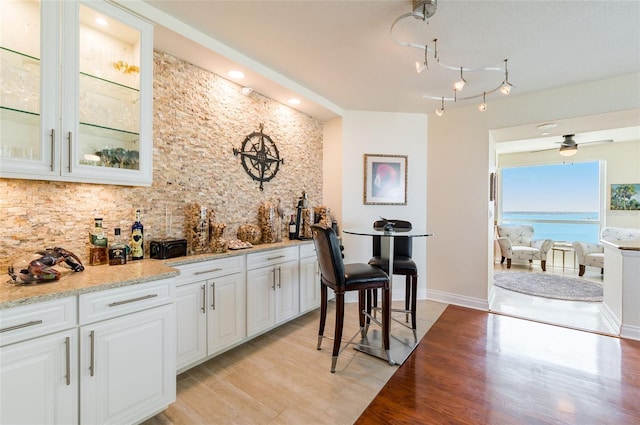 kitchen with white cabinets, light stone countertops, light wood-type flooring, ceiling fan, and a water view