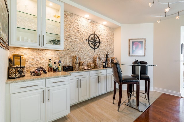 bar with light stone counters, light hardwood / wood-style flooring, track lighting, and white cabinetry