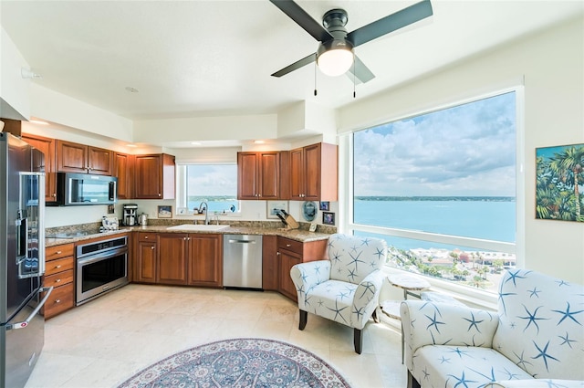 kitchen featuring light tile patterned floors, stainless steel appliances, a water view, ceiling fan, and sink