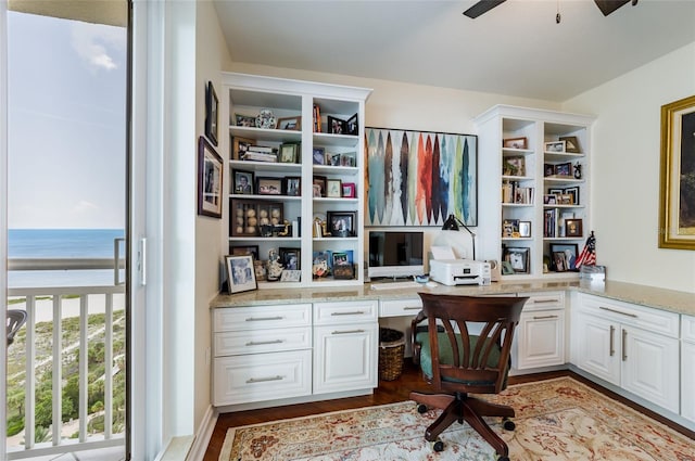 home office featuring ceiling fan, a water view, hardwood / wood-style flooring, and built in desk