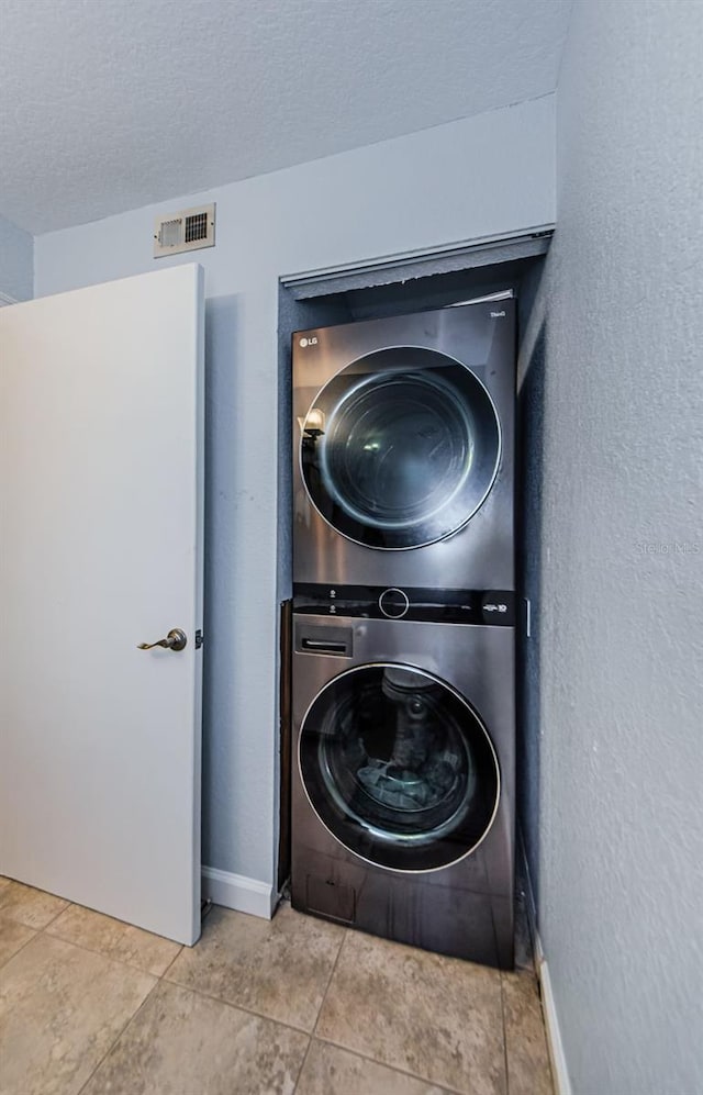 washroom with stacked washer / drying machine, tile patterned floors, and a textured ceiling