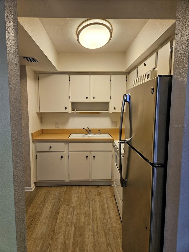 kitchen featuring white cabinetry, stainless steel refrigerator, hardwood / wood-style flooring, sink, and stove