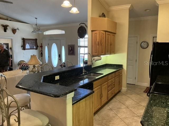 kitchen with dark stone countertops, black refrigerator, light tile patterned floors, decorative light fixtures, and sink