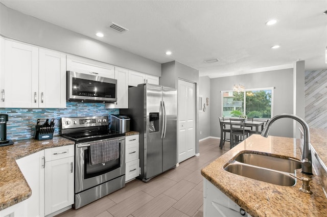 kitchen with stainless steel appliances, a sink, visible vents, white cabinetry, and light stone countertops