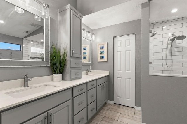 bathroom featuring a sink, double vanity, a tile shower, and a closet