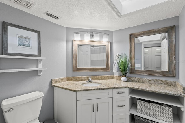 bathroom featuring visible vents, vanity, toilet, and a textured ceiling