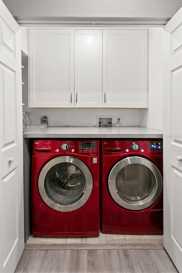 clothes washing area featuring light wood-style flooring, cabinet space, and washer and clothes dryer