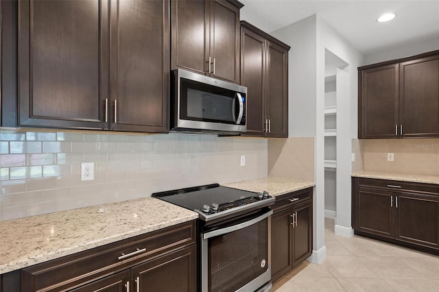 kitchen featuring appliances with stainless steel finishes, light tile patterned flooring, dark brown cabinetry, and light stone countertops