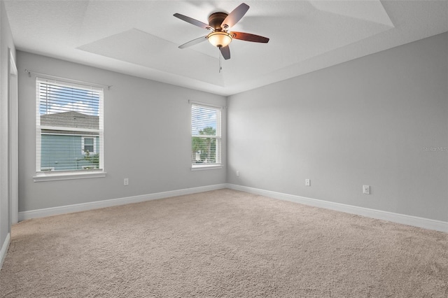 spare room featuring a tray ceiling, carpet flooring, ceiling fan, and baseboards