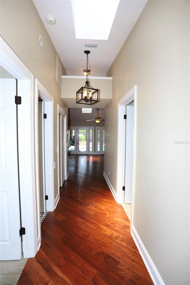 hall with a notable chandelier, a skylight, and dark wood-type flooring