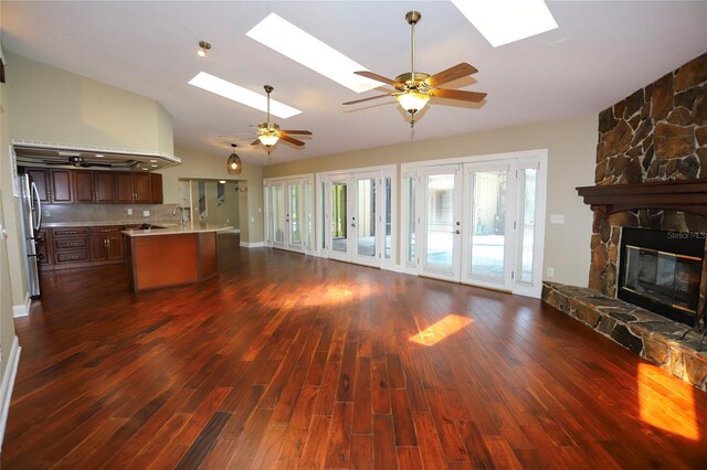 unfurnished living room with vaulted ceiling with skylight, a fireplace, french doors, and dark hardwood / wood-style floors