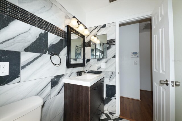 bathroom featuring backsplash, wood-type flooring, vanity, tile walls, and toilet