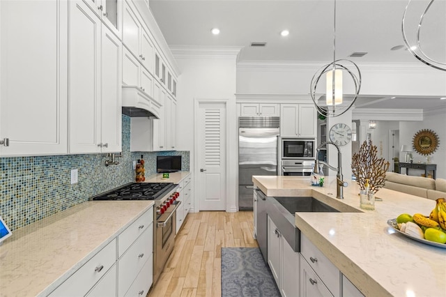 kitchen with built in appliances, light wood-type flooring, tasteful backsplash, and crown molding