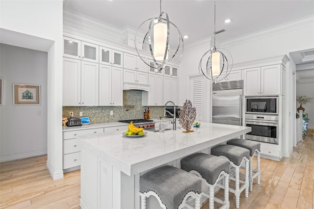 kitchen featuring pendant lighting, an island with sink, built in appliances, backsplash, and light hardwood / wood-style flooring