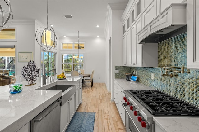 kitchen with appliances with stainless steel finishes, custom exhaust hood, backsplash, ornamental molding, and light hardwood / wood-style floors