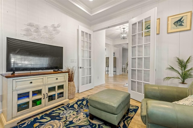 living area with light wood-type flooring, french doors, ornamental molding, and a tray ceiling