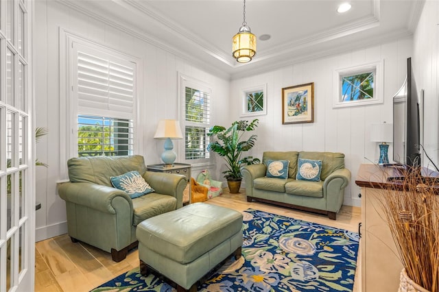 living room featuring light wood-type flooring, ornamental molding, and a tray ceiling