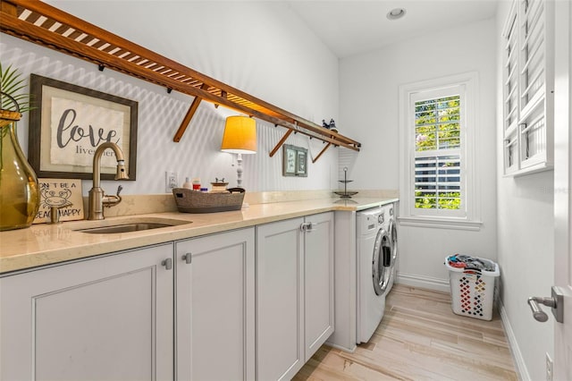 laundry room with sink, light hardwood / wood-style flooring, washing machine and clothes dryer, and cabinets