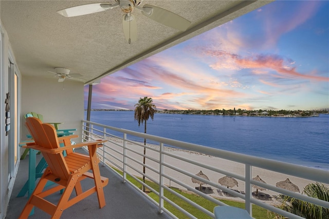 balcony at dusk with a water view and ceiling fan