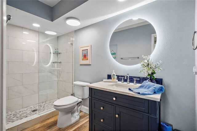 bathroom featuring wood-type flooring, a tile shower, vanity, and toilet