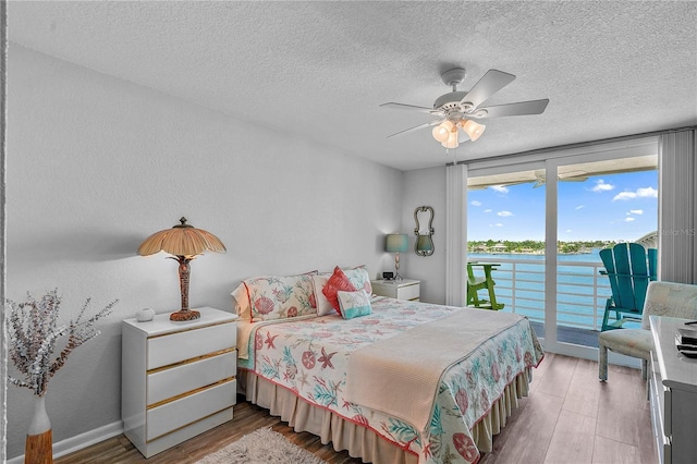 bedroom with access to exterior, hardwood / wood-style floors, floor to ceiling windows, and a water view