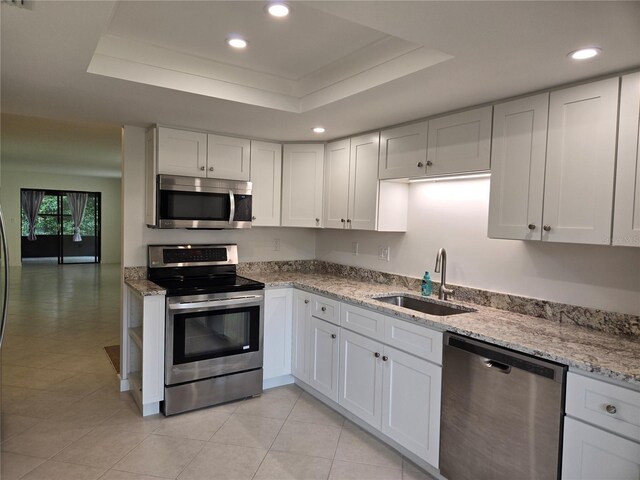 kitchen featuring a raised ceiling, white cabinets, appliances with stainless steel finishes, light stone counters, and sink