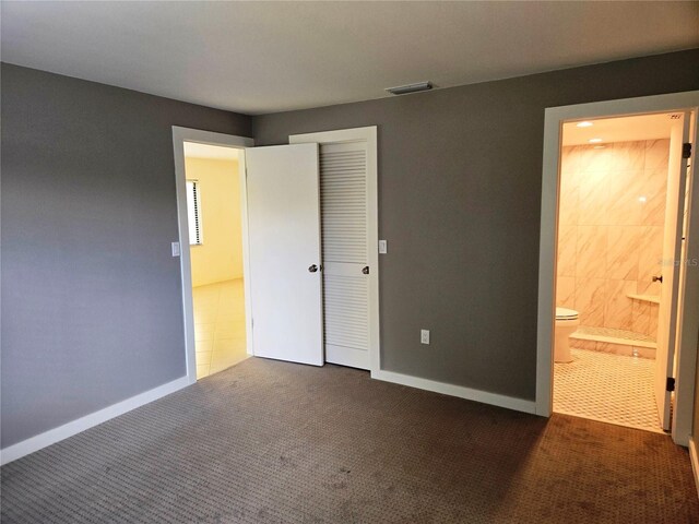 unfurnished bedroom with ensuite bathroom, dark carpet, and a closet