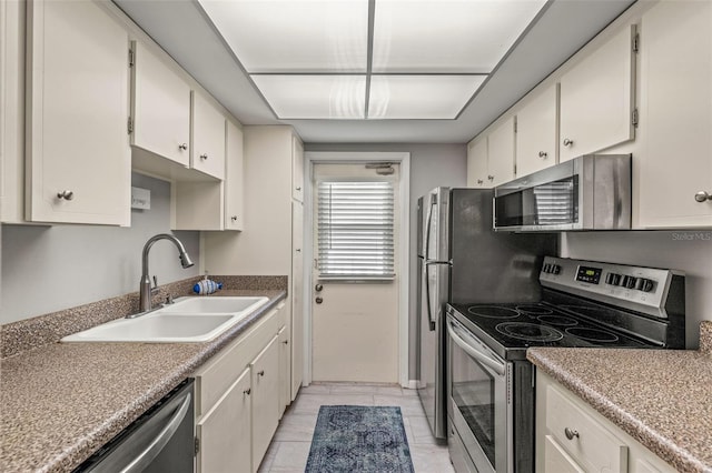 kitchen with sink, stainless steel appliances, light tile patterned flooring, and white cabinetry