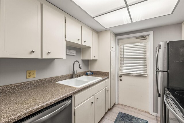 kitchen with light tile patterned flooring, sink, range, stainless steel dishwasher, and white cabinets