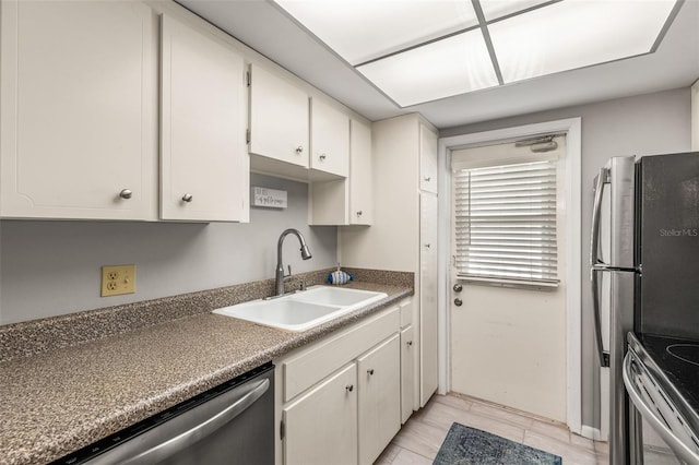 kitchen with appliances with stainless steel finishes, dark countertops, a sink, and white cabinets