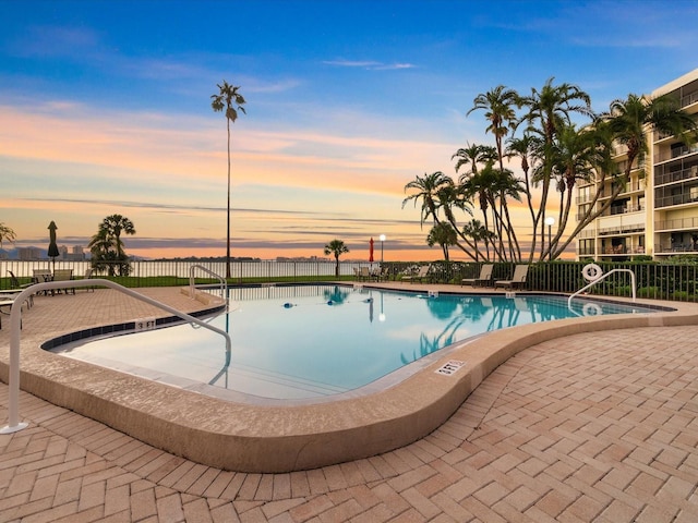 pool at dusk with a water view and a patio