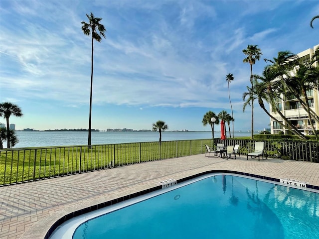 view of pool featuring a water view, a patio area, and a lawn