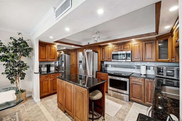 kitchen featuring tasteful backsplash, dark stone counters, a kitchen island, ceiling fan, and stainless steel appliances