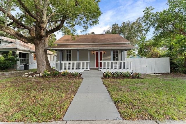 bungalow-style house featuring fence, a shingled roof, covered porch, and a front yard