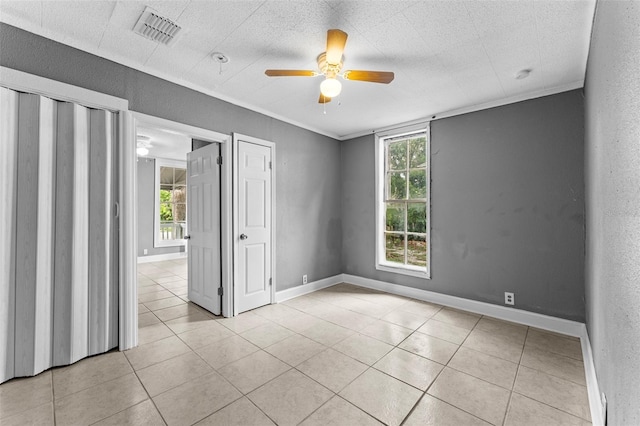 empty room featuring ceiling fan, light tile patterned flooring, a healthy amount of sunlight, and crown molding