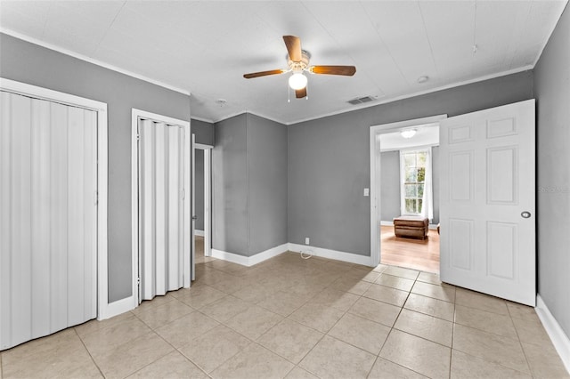 unfurnished bedroom with ceiling fan, light tile patterned flooring, ornamental molding, and multiple closets