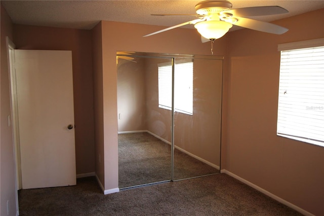 unfurnished bedroom featuring multiple windows, a closet, dark colored carpet, and ceiling fan