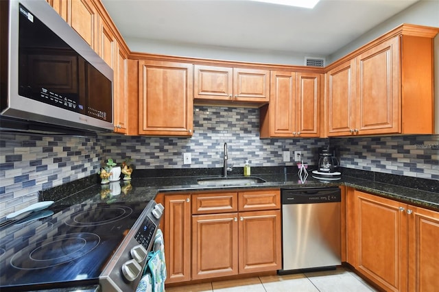 kitchen featuring sink, light tile patterned floors, backsplash, stainless steel appliances, and dark stone counters