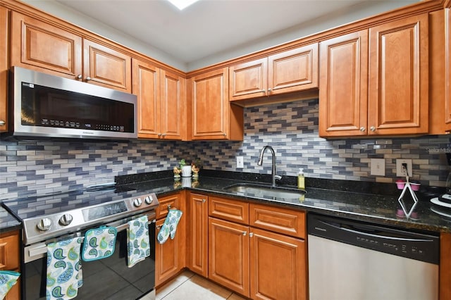 kitchen featuring light tile patterned flooring, appliances with stainless steel finishes, sink, dark stone countertops, and decorative backsplash