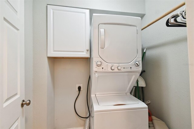 laundry room featuring stacked washer / drying machine and cabinets