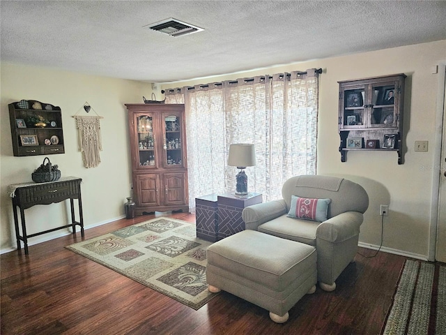 living area featuring a textured ceiling, wood finished floors, visible vents, and baseboards