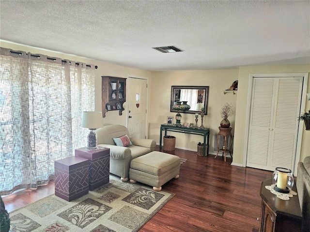 living area featuring baseboards, a textured ceiling, visible vents, and wood finished floors