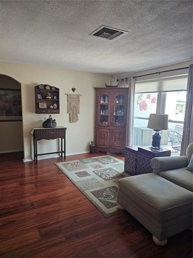 living area featuring a textured ceiling, wood finished floors, visible vents, and baseboards