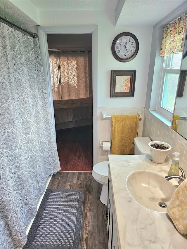 ensuite bathroom with tile walls, toilet, wainscoting, ensuite bath, and wood finished floors