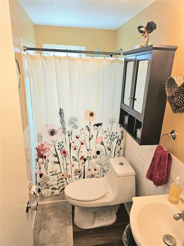 bathroom with a shower with curtain, a sink, toilet, and tile walls